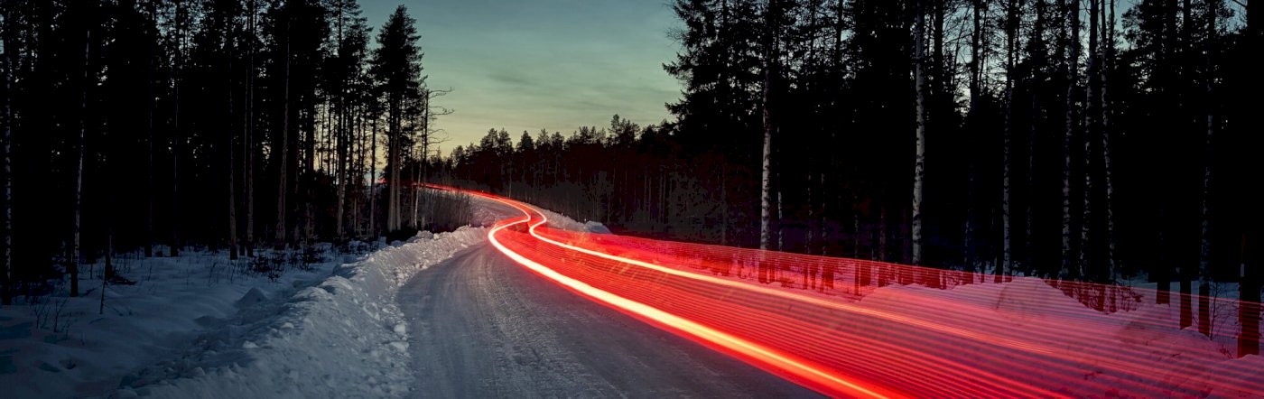 Roter Lichtstreifen, verursacht durch die Rücklichter eines Volvo zieht sich durch einen verschneiten Wald